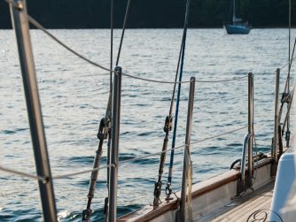 safety stays on a sail boat with water beyond and a anchored sail boat in the background with a back drop of lush green trees cursive JTL in circle water mark in the lower right corner