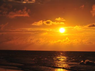 golden sunrise over the gulf of Mexico with cursive JTL Logo in the bottom Right corner