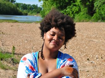 Jamelah hugging herself on a river beach.